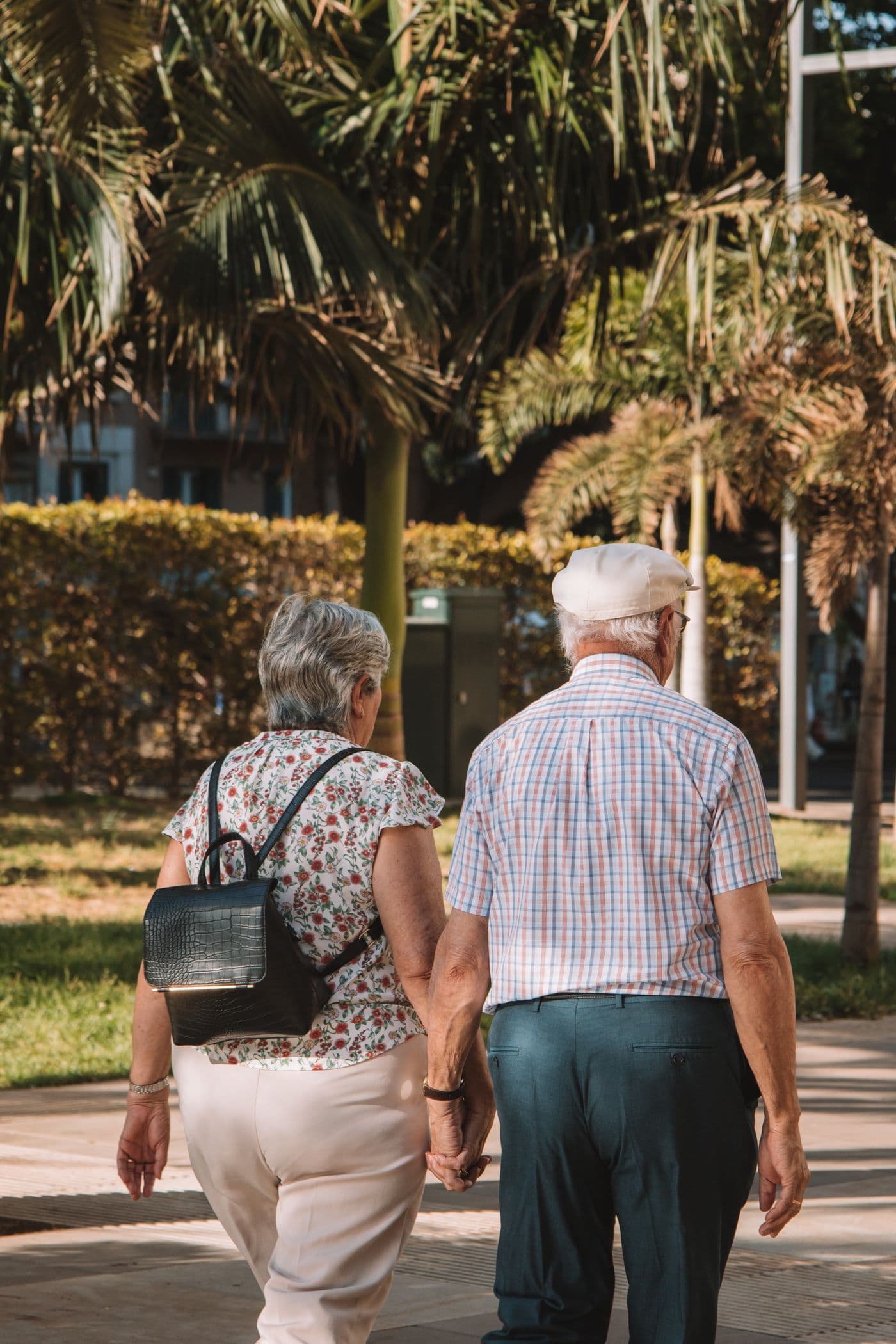 An older couple walking hand in hand along a sunny park path